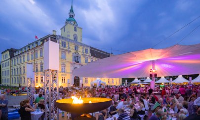 Vor dem Oldenburger Schloss sitzen viele Besucher bei der Veranstaltung Kochen am Schloss unter einem großen Sonnentuch.