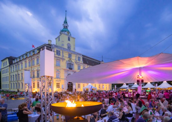 Vor dem Oldenburger Schloss sitzen viele Besucher bei der Veranstaltung Kochen am Schloss unter einem großen Sonnentuch.