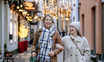 Bild von zwei lächelnden Frauen beim Weihnachtsshopping in der festlich beleuchteten Bergstraße in Oldenburg.