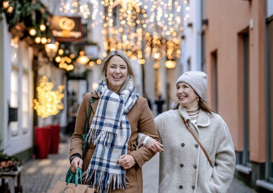 Bild von zwei lächelnden Frauen beim Weihnachtsshopping in der festlich beleuchteten Bergstraße in Oldenburg.