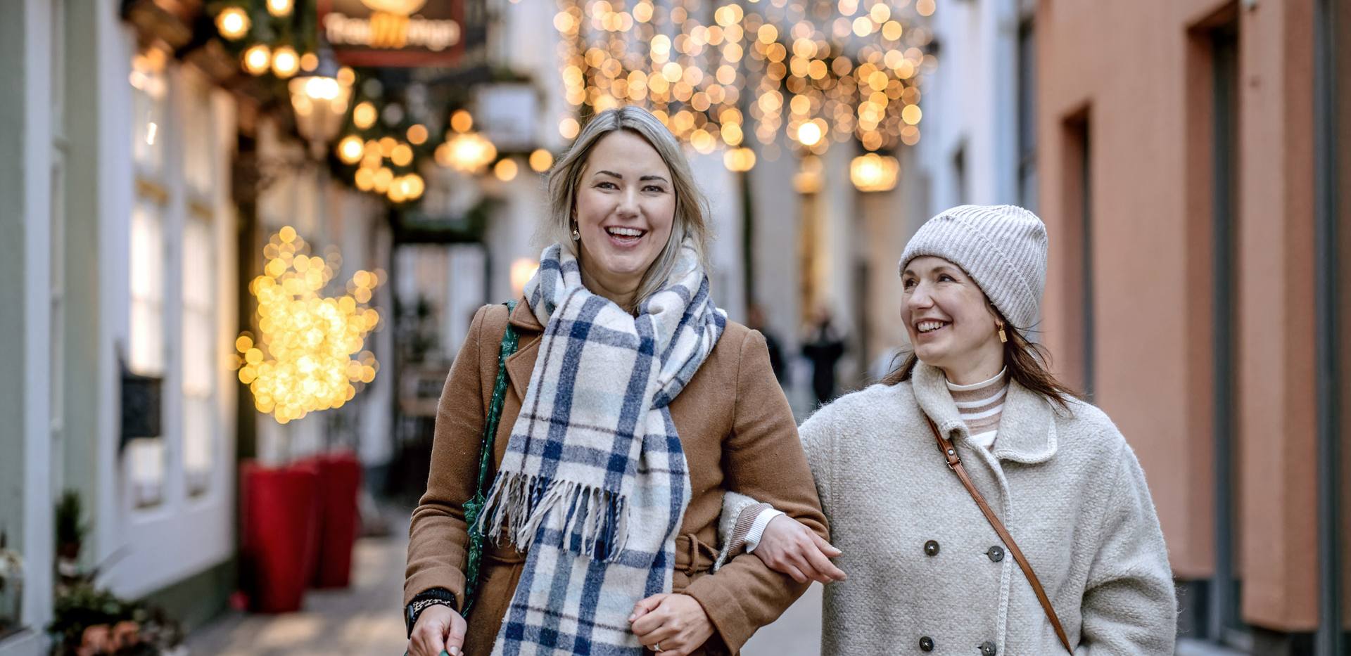 Bild von zwei lächelnden Frauen beim Weihnachtsshopping in der festlich beleuchteten Bergstraße in Oldenburg.
