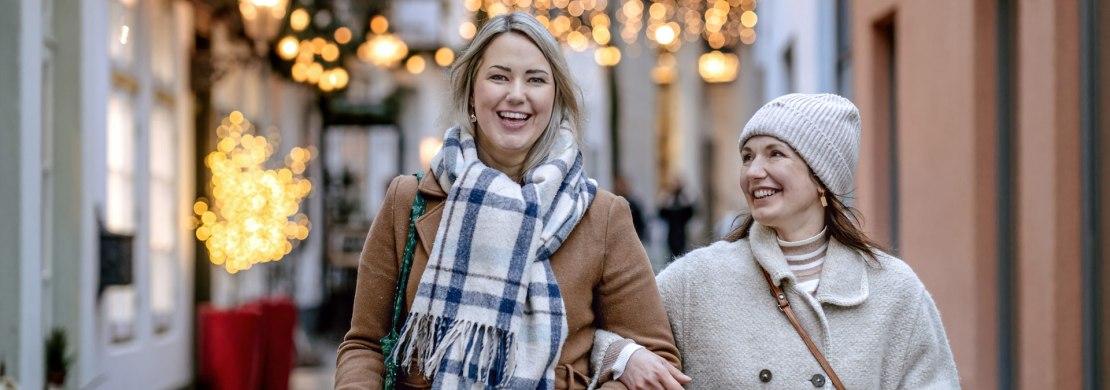 Bild von zwei lächelnden Frauen beim Weihnachtsshopping in der festlich beleuchteten Bergstraße in Oldenburg.