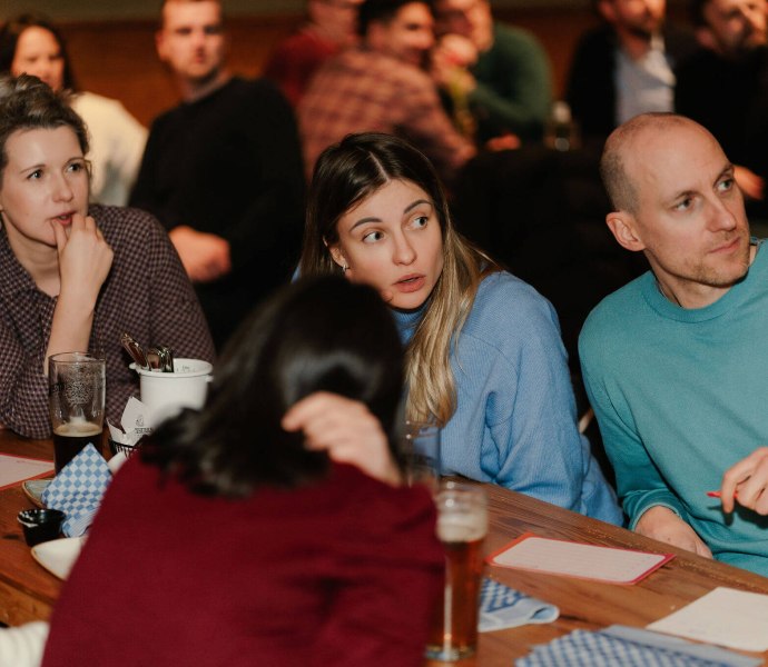 Drei Freunde nicken und diskutieren lebhaft, während sie die nächste knifflige Frage beim Pubquiz lösen.