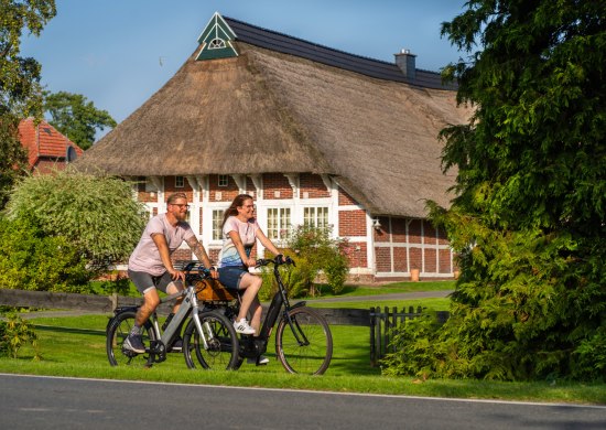 Radfahrer auf der Route um Oldenburg vor einem Reetdachhaus in Wesermarsch