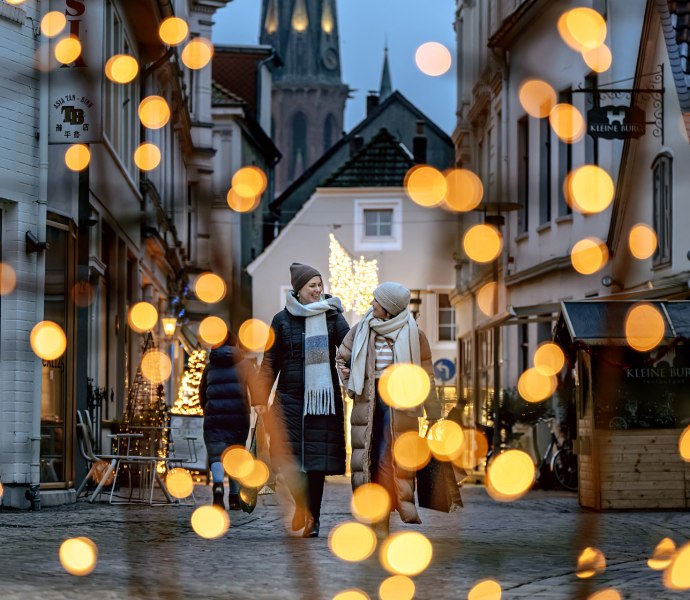 Zwei Frauen gehen durch die weihnachtlich beleuchtete Burgstraße in Oldenburg. 